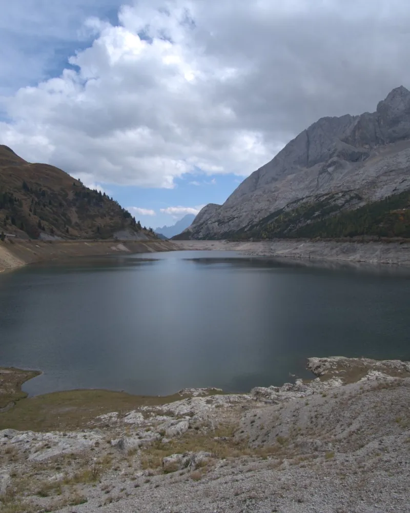 Lago artificiale sotto montagne grigie, con la riva di sassi in primo piano